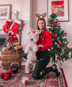 Woman & Westie dog wearing matching antlers with christmas tree and stockings in the background